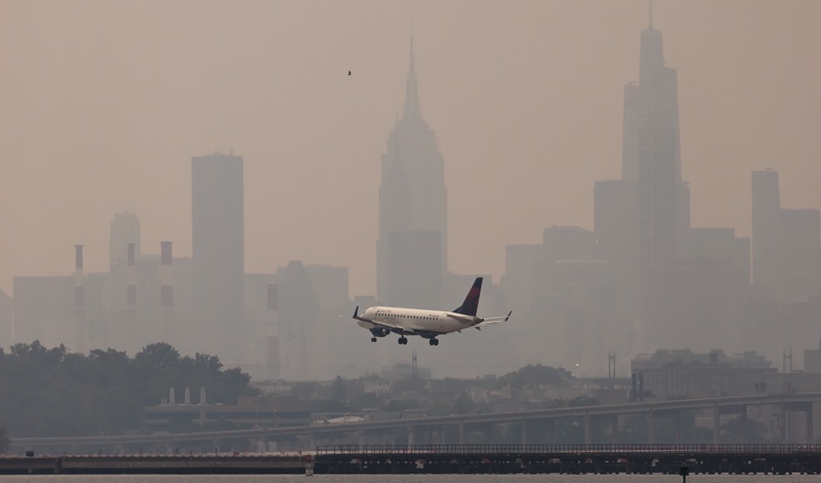 A plane is about to land at LaGuardia airport in New York.  with the Manhattan skyline in the background amid smoke from the wildfires burning in Canada