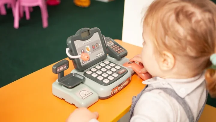 A child's hand holding an iPhone, simulating an Apple Pay transaction with a blurred background