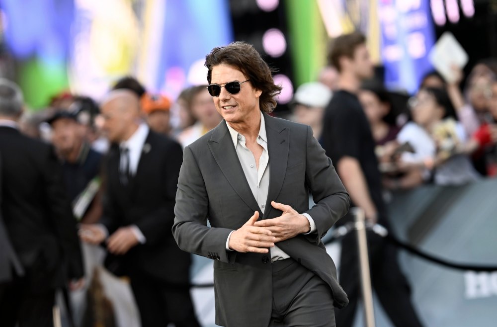 Tom Cruise smiling and waving, wearing a suit.